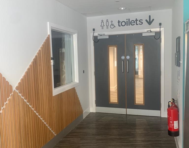 Commercial hallway with a timber slat wall, grey toilet doors and dark wood-effect flooring
