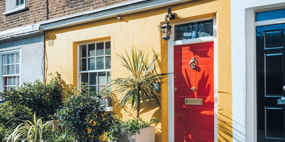 Yellow rendered terrace front with a high-gloss red door and white sash window